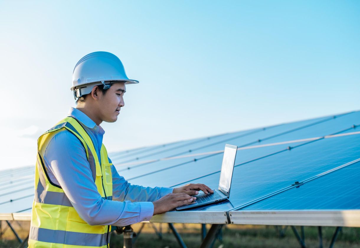 Worker inspecting solar panels with laptop.
